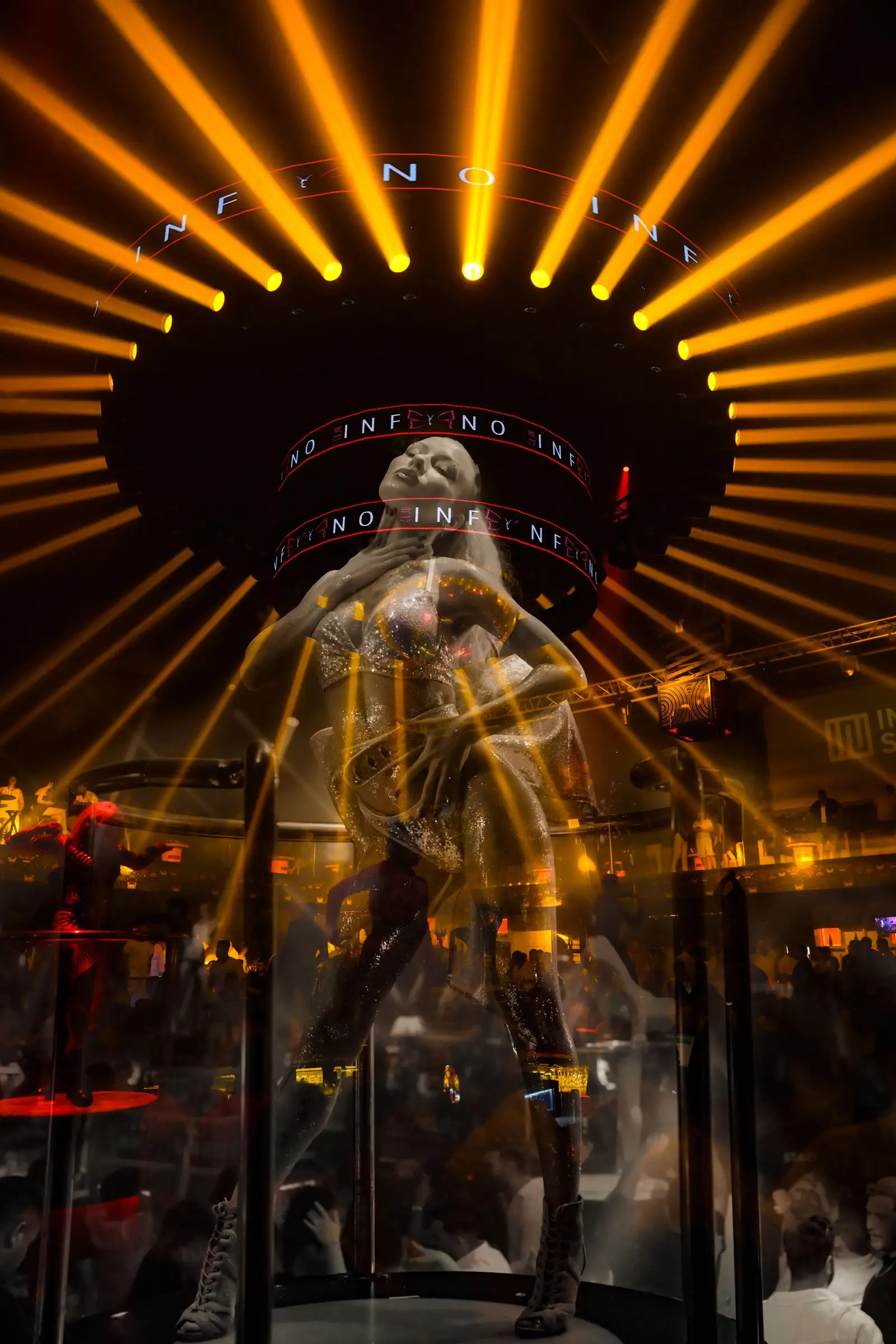 Gece kulübünde turuncu ışık huzmeleri altında platform üzerinde dans eden performans sanatçısı